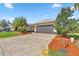 Home exterior featuring a two-car garage, paver driveway, and mature trees on a sunny day at 10138 Lake Miona Way, Oxford, FL 34484