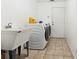 Bright laundry room with white washer and dryer, a utility sink, white walls, and tile flooring at 3994 Sw 102Nd Pl, Ocala, FL 34476