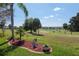 Manicured backyard overlooking lush green golf course, enhanced by a decorative flowerbed, and palm trees at 13544 Se 89Th Terrace Rd, Summerfield, FL 34491