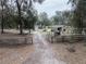 A gated gravel drive extends toward an outbuilding and other buildings on a treed lot at 5490 Se Highway 42, Summerfield, FL 34491