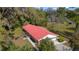 Aerial view of a red-roofed home with an attached garage and a covered patio surrounded by mature trees and a green lawn at 1300 Ne 53Rd St, Ocala, FL 34479