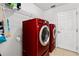 A laundry room features modern red washer and dryer units with a white shelf and a door at 17 Pine Course Loop, Ocala, FL 34472