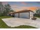 Home exterior with a spacious three car garage and modern doors, set against a colorful sunset at 4869 Nw 101St Street Rd, Ocala, FL 34482
