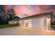 Spacious three-car garage with modern doors and ample parking space, complemented by a lovely sunset backdrop at 4869 Nw 101St Street Rd, Ocala, FL 34482