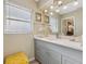 Bathroom with a single sink vanity, large mirror, neutral colored walls, window, and a yellow chair at 9305 Bahia Track Way, Ocala, FL 34472
