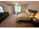 Bright main bedroom with a large window, ceiling fan, carpet, and dark wood furniture at 15055 Se 93Rd Ct, Summerfield, FL 34491
