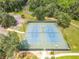 Aerial view of well-maintained tennis courts, featuring a fenced perimeter, lighting, and surrounding landscape at 19533 Sw 86Th Ln, Dunnellon, FL 34432