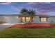 Charming home exterior with manicured lawn, colorful mulch, and young palm trees at dusk at 2013 Cardona Way, The Villages, FL 32159