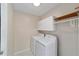 Bright laundry room featuring white washer and dryer, overhead cabinets, and wooden shelf with hanging rod at 2013 Cardona Way, The Villages, FL 32159