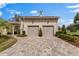 A two-car garage featuring stone accents, beautiful landscaping, and brick driveway at 12424 Sw 140Th Loop, Dunnellon, FL 34432