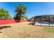 View of a backyard with grass, trees, red fence, and a screened in pool at 5041 Ne 4Th St, Ocala, FL 34470