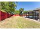 View of a backyard with patchy grass, trees, red fence, and a screened in pool at 5041 Ne 4Th St, Ocala, FL 34470