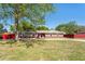 Single-story home featuring a red fence, well-maintained lawn, and large tree providing shade at 5041 Ne 4Th St, Ocala, FL 34470