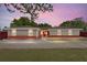 Charming ranch-style home with a brick facade and a well-manicured lawn under a pink and purple sky at 5041 Ne 4Th St, Ocala, FL 34470