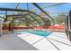View of a pool with screened enclosure, concrete pool deck, and large trees at 5041 Ne 4Th St, Ocala, FL 34470