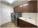 Laundry room features a washer, dryer, sink, cabinets, tiled floor and a white door at 6307 Se 8Th Ln, Ocala, FL 34472
