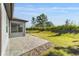 Back patio extending into a lush green backyard, partially bordered by tall hedges and trees under a clear blue sky at 5870 Sw 93Rd Cir, Ocala, FL 34481