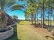 Wide backyard view showing lush green lawn, stone retaining wall and mature trees, with golf course in background at 7527 Sw 97Th Terrace Rd, Ocala, FL 34481