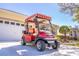 Red and tan golf cart parked on the driveway in front of a home, sunny day at 9458 Sw 93Rd Loop, Ocala, FL 34481