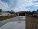 Tan, one-story home with a dark garage door, long driveway and partially cloudy sky at 13 Locust Trak, Ocala, FL 34472
