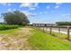 White horse barn with a metal roof and several stalls, complemented by green grass, landscaping, and trees at 13800 Ne Jacksonville Road, Citra, FL 32113