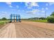 View of a dirt racetrack with a blue metal horse racing starting gate, white fence and outbuildings with a blue sky backdrop at 13800 Ne Jacksonville Road, Citra, FL 32113