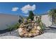 Landscaped backyard rock waterfall feature with lush plantings and blue sky backdrop at 7014 Elaine Ct, The Villages, FL 34762