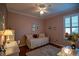 A cozy bedroom featuring wood floors, light pink walls, a ceiling fan, a desk and large window at 13968 Se 96Th Cir, Summerfield, FL 34491