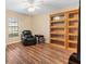 A bonus room featuring hardwood floors, a window with blinds, a chair, and beautiful wall shelving at 12240 Se 172Nd Ln, Summerfield, FL 34491