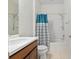 Bright bathroom with a single sink vanity, toilet, and bathtub with shower featuring a blue and white curtain at 7665 Sw 96Th Avenue Rd, Ocala, FL 34481