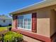 Close-up of a window with red shutters, showing well-maintained landscaping and exterior paint at 11395 Sw 139Th St, Dunnellon, FL 34432