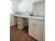 Well-lit laundry room with white cabinets, countertop, sink, and storage shelves, complemented by wood-look flooring at 8214 Nw 17Th Cir, Ocala, FL 34475