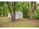Exterior view of a white storage shed nestled among trees in a lush backyard at 5118 Sw 197Th Ter, Dunnellon, FL 34431
