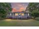 Cozy single-story home with a welcoming front porch, featuring green shutters and lush landscaping at sunset at 2720 Se 145Th St, Summerfield, FL 34491