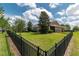 Large backyard with a black metal fence, green grass, mature trees, and view of the home's rear exterior at 4945 Nw 35Th Lane Rd, Ocala, FL 34482