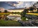 Scenic view of a golf course pond reflecting a vibrant sunset, framed by rocks and lush greenery at 5195 Nw 21St Loop, Ocala, FL 34482