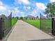 View through the gate of a sprawling estate featuring a luxurious home and manicured lawn at 7161 Ne 22Nd Court Rd, Ocala, FL 34479