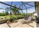 Screened patio features a lounge chair, lush tropical plants, and a view of the well-manicured lawn at 7855 Sw 97Th Cir, Ocala, FL 34481