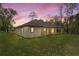 View of the house's backyard during sunset featuring green grass, a covered patio and mature trees at 19939 Sw 96Th Pl, Dunnellon, FL 34432
