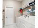 Bright laundry room with white washer and dryer, storage shelves, and white door with marble tile flooring at 10033 Sw 96Th St, Ocala, FL 34481