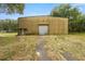 Exterior shot of large metal barn with roll up door, side entrance, and overgrown front yard at 3360 Se 183Rd Avenue Rd, Ocklawaha, FL 32179