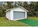 A detached garage with a gray door, white siding, and adjacent green Astroturf offers extra storage at 9900 Ne 20 Terrace Rd, Anthony, FL 32617