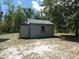 A gray shed is nestled in a treed backyard on a sunny day at 20364 Sw 86Th Loop, Dunnellon, FL 34431
