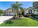 Inviting home exterior featuring lush green lawn, a palm tree, and a brick driveway leading to a two-car garage at 9443 Sw 71St Loop, Ocala, FL 34481