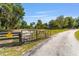Property entrance with a gated driveway, lush landscaping, and a charming home in the distance at 18695 Ne 5Th Terrace Rd, Citra, FL 32113