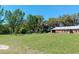 Large green lawn leading to a rustic red barn with abundant trees and a clear blue sky in the background at 2630 Nw 140Th St, Citra, FL 32113