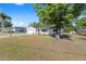 Single-story home with a white exterior, attached garage, and a well-maintained lawn, shaded by a large tree at 614 Third Ave, Lady Lake, FL 32159