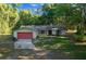 Cozy single-Gathering home featuring a red garage door, complemented by a green lawn and mature trees at 16571 Se 95Th Street Rd, Ocklawaha, FL 32179