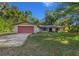 Charming single-story home with a well-maintained lawn and mature trees, featuring a red garage door at 16571 Se 95Th Street Rd, Ocklawaha, FL 32179