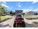 Image of a red golf cart parked on a brick driveway, with houses visible in the background under a blue sky at 10327 Sw 96Th Loop, Ocala, FL 34481